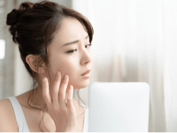 鏡を見ながら肌の状態を気にする女性の写真。エイジングケアを考える姿をイメージ