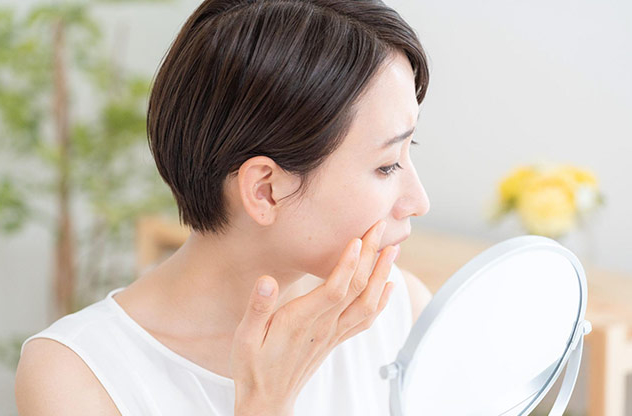 鏡を使いながら頬に触れてスキンケアを確認している女性の姿