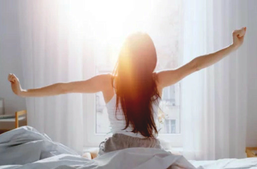 体内時計を整えるために、朝日を浴びながら目覚める女性のイメージ